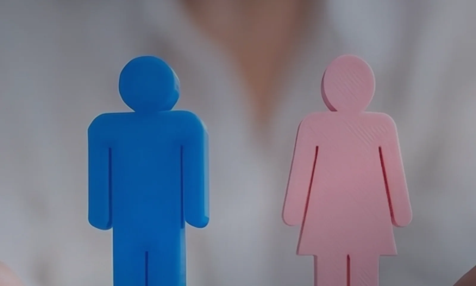 Figuras de um homem e de uma mulher sobre pilhas de moedas de mesma altura, representando igualdade salarial